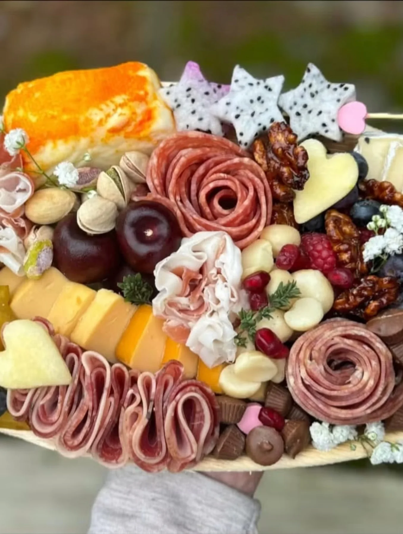 Appetizing signature charcuterie board with salami roses, heart-shaped cheese, fruit, and sweets