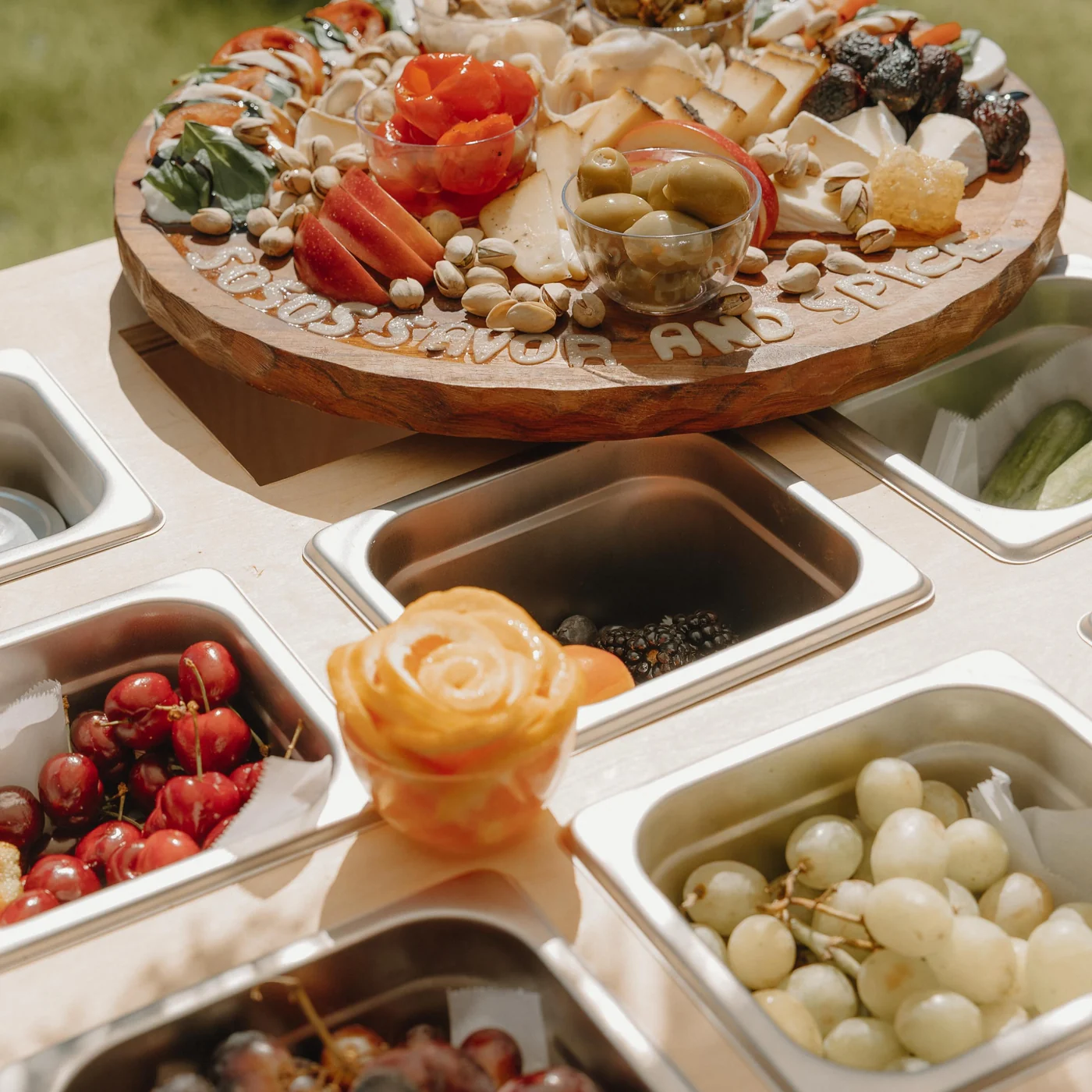Curated outdoor charcuterie board with cheeses, fruit, olives, honeycomb, and pistachios